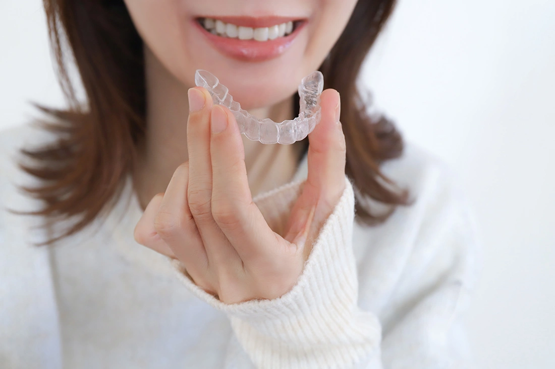 A woman smiling as she holds onto her clear aligners